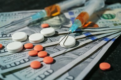 Photo of Drug addiction. Dollar banknotes, pills and syringes on black table, closeup