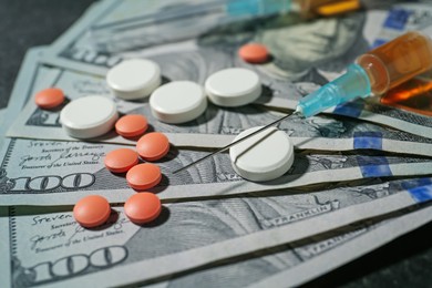 Photo of Drug addiction. Dollar banknotes, pills and syringe on gray table, closeup