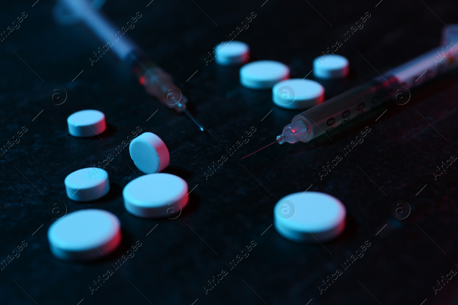 Photo of Drug addiction. Pills and syringes on dark textured table in neon lights, closeup