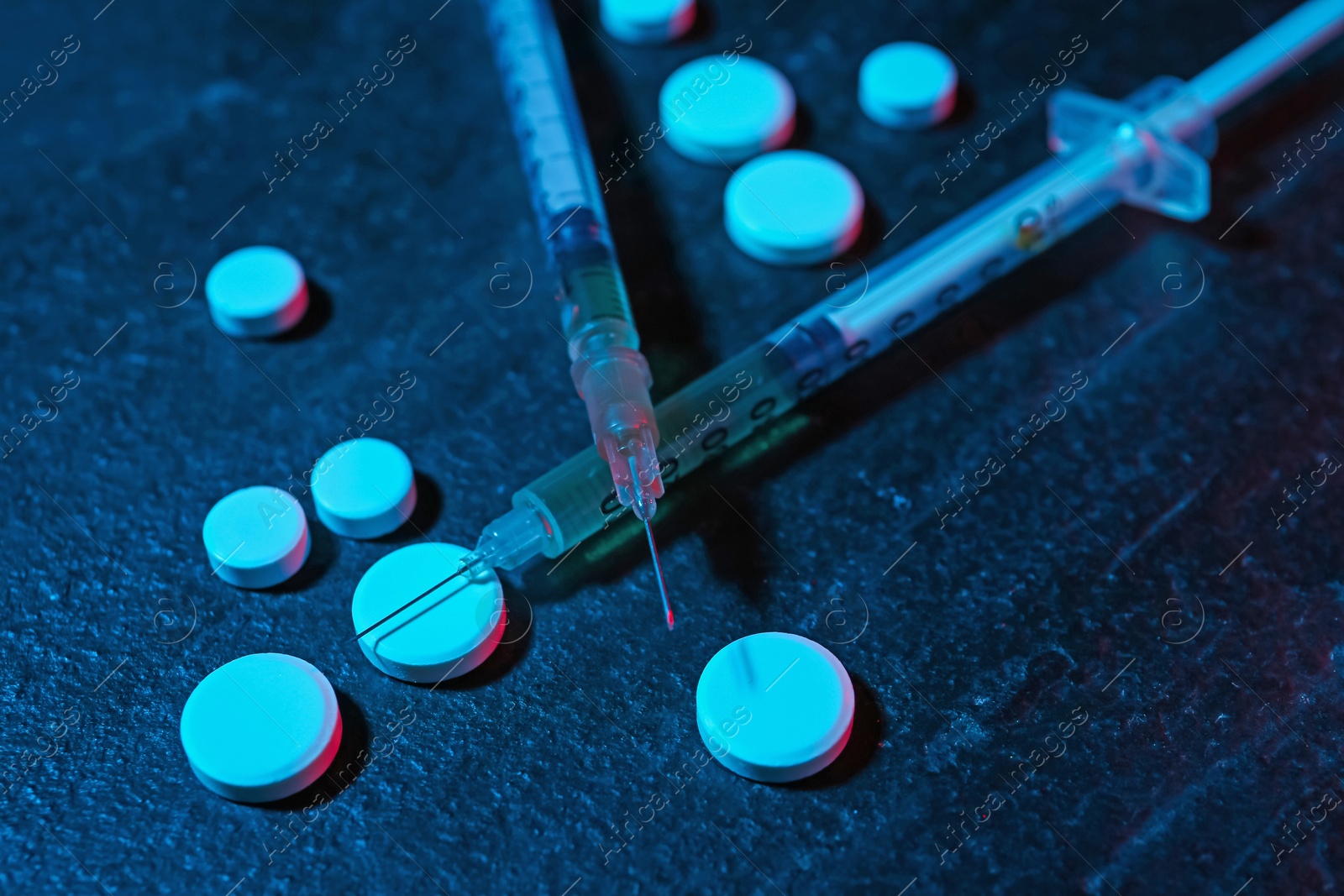 Photo of Drug addiction. Pills and syringes on dark textured table in neon lights, closeup