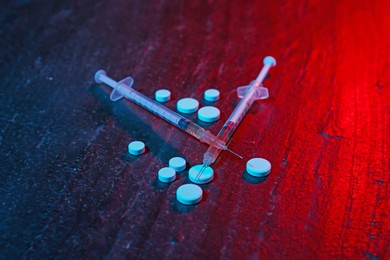 Photo of Drug addiction. Pills and syringes on dark textured table in neon lights