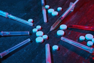 Photo of Drug addiction. Pills and syringes on dark textured table in neon lights, closeup