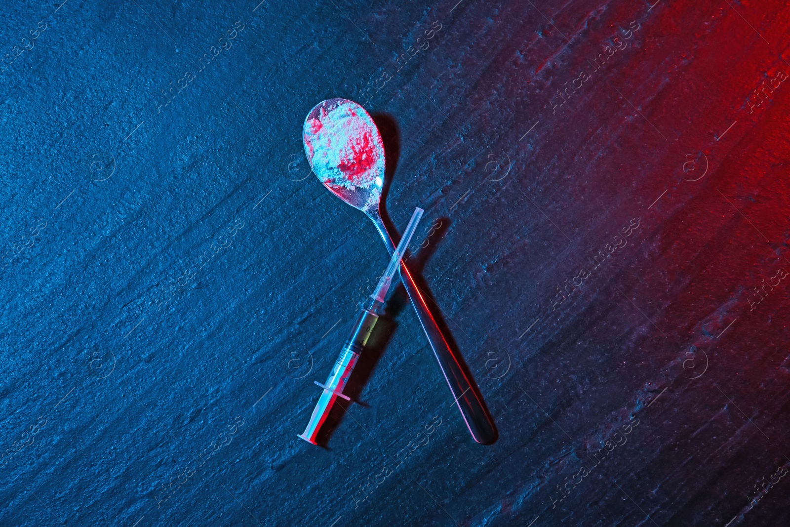 Photo of Drug addiction. Spoon with powder and syringe on dark textured table in neon lights, flat lay