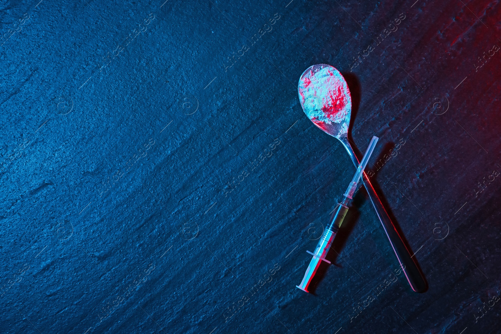 Photo of Drug addiction. Spoon with powder and syringe on dark textured table in neon lights, flat lay. Space for text