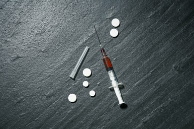 Photo of Drug addiction. Syringe and pills on dark textured table, flat lay