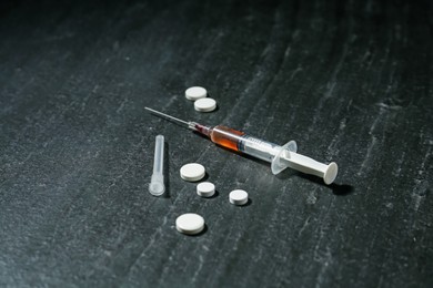 Photo of Drug addiction. Syringe and pills on dark textured table