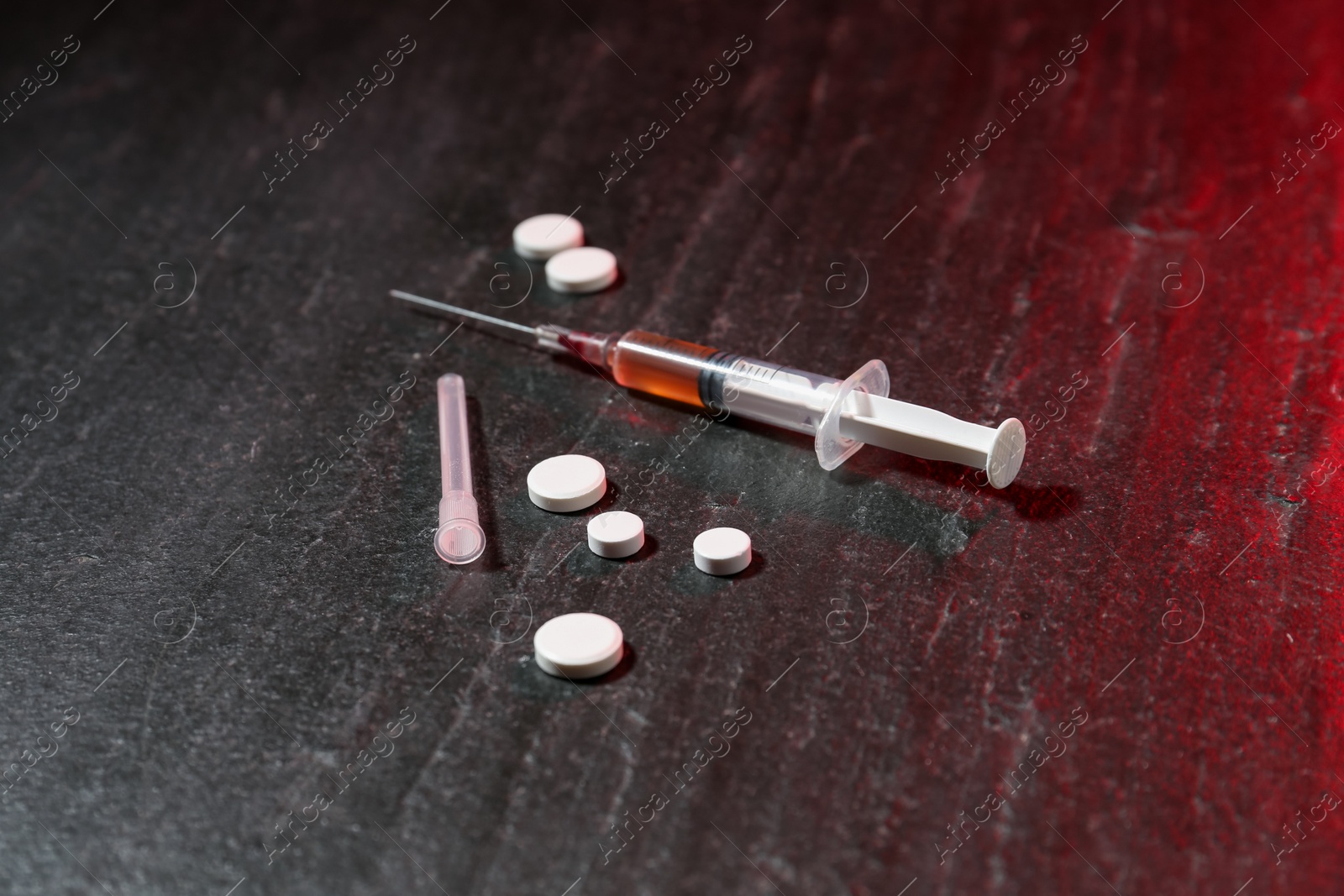 Photo of Drug addiction. Syringe and pills on dark textured table in color light