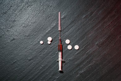 Photo of Drug addiction. Syringe and pills on dark textured table, flat lay