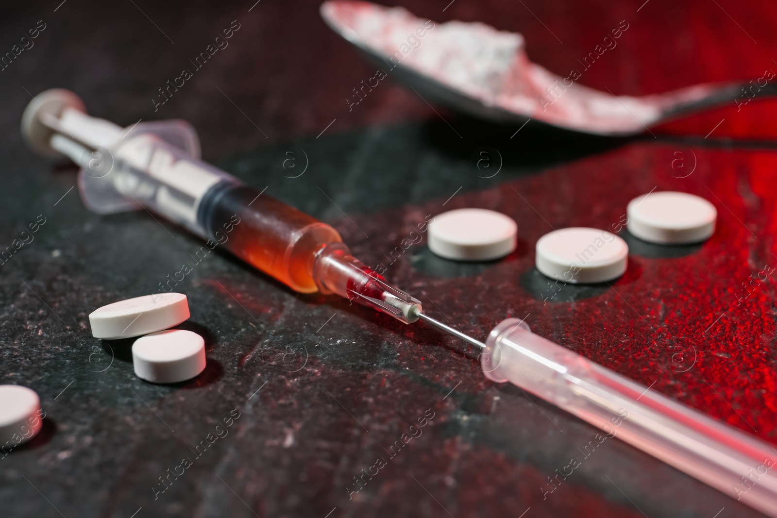 Photo of Drug addiction. Syringe and pills on dark textured table in color light, closeup