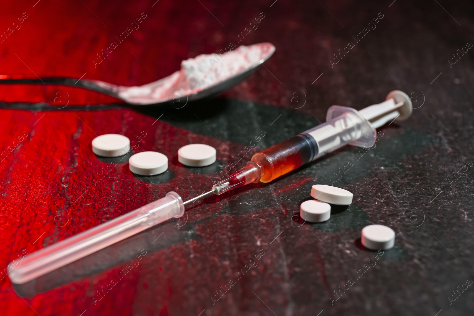 Photo of Drug addiction. Syringe, pills and spoon with powder on dark textured table in color light, closeup