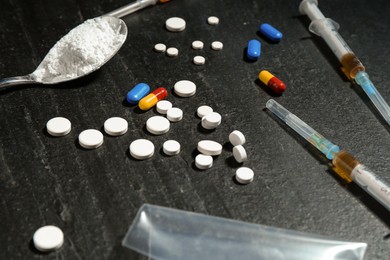 Photo of Drug addiction. Pills, syringes and spoon with powder on dark textured table, closeup