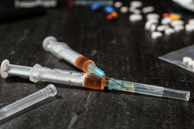 Photo of Drug addiction. Syringes and pills on dark textured table, closeup