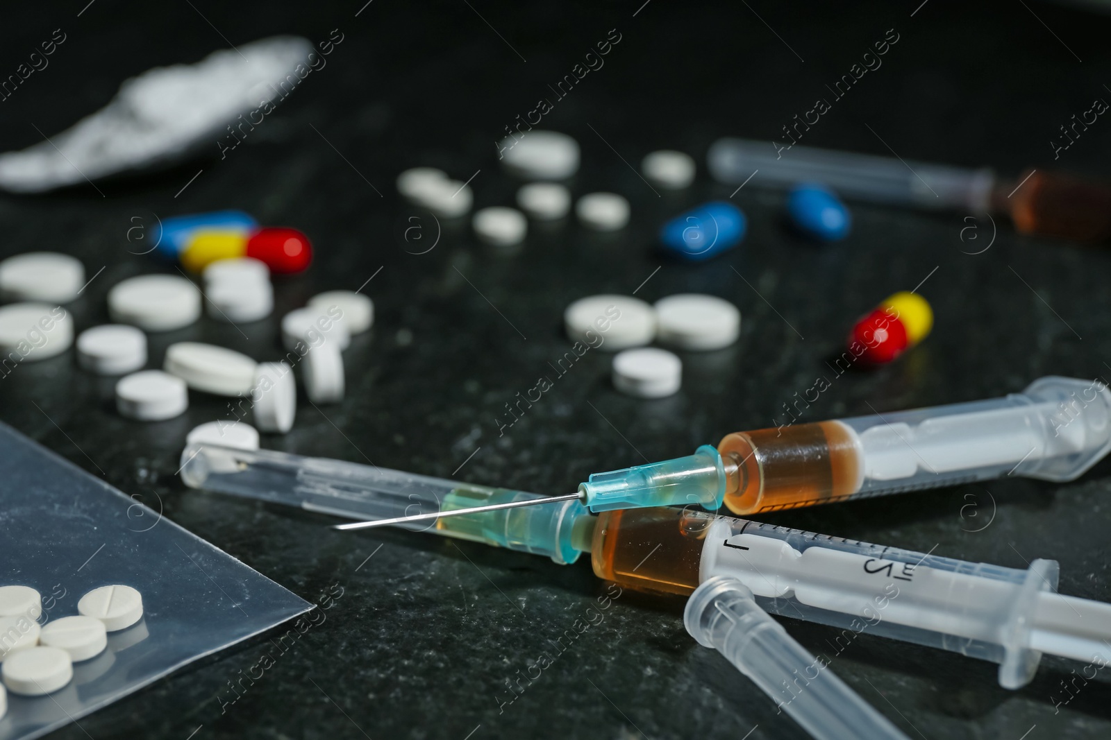 Photo of Drug addiction. Syringes and pills on dark textured table, closeup