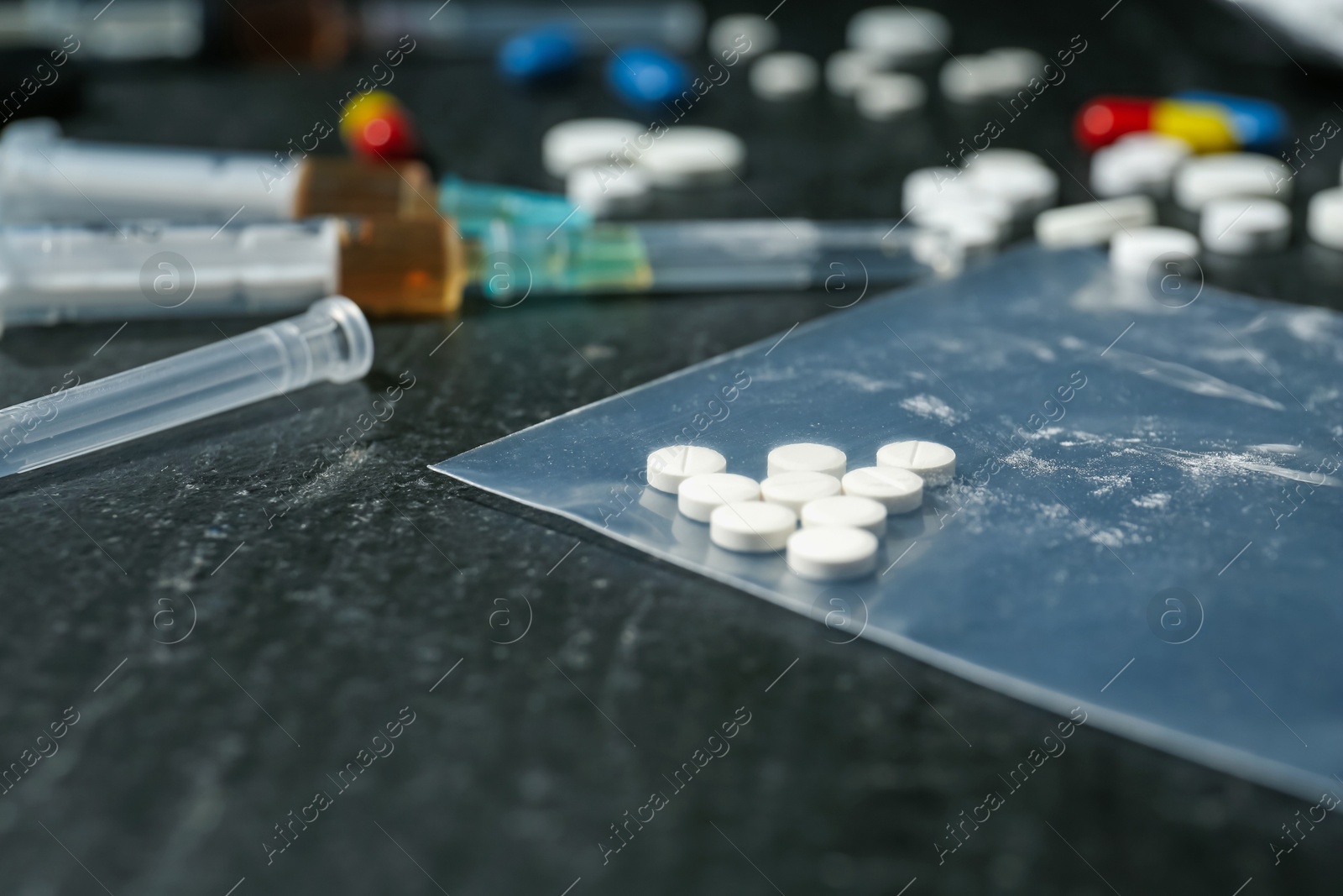 Photo of Drug addiction. Plastic bag with pills and syringes on dark textured table, closeup