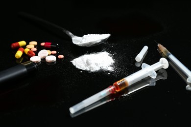 Photo of Drug addiction. Syringes, spoon with powder and pills on black table