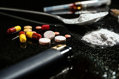 Photo of Drug addiction. Spoon with powder, pills and cigarette lighter on black table, closeup