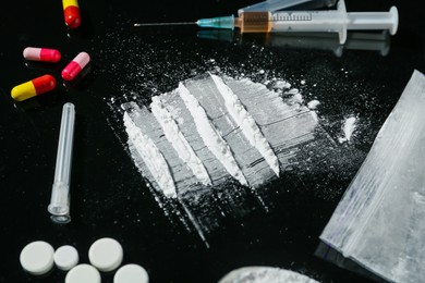 Photo of Drug addiction. Powder, pills and syringe on black table, closeup