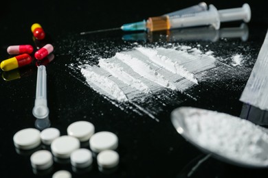 Photo of Drug addiction. Powder, pills and syringe on black table, closeup