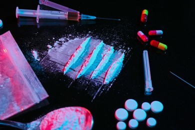 Photo of Drug addiction. Plastic bag with powder, pills, syringe and spoon on black table in neon lights, closeup