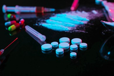 Photo of Drug addiction. Pills and powder on black table in neon lights, closeup