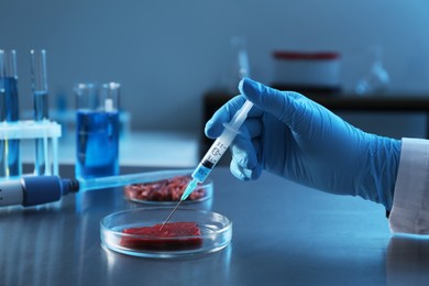 Photo of GMO concept. Scientist injecting something into piece of meat at table in laboratory, closeup