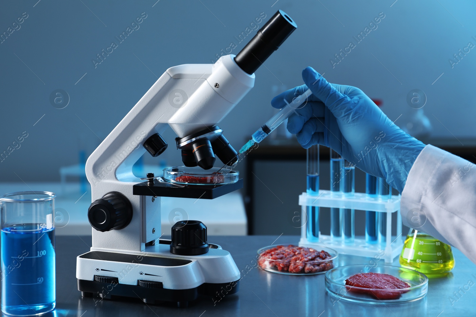 Photo of GMO concept. Scientist injecting something into piece of meat under microscope in laboratory, closeup