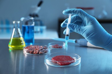 Photo of GMO concept. Scientist injecting something into piece of meat at table in laboratory, closeup