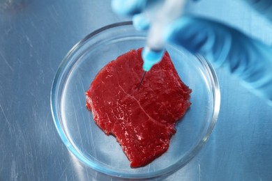 Photo of GMO concept. Scientist injecting something into piece of meat at table, above view