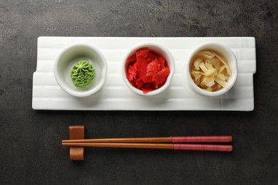 Photo of Hot wasabi paste, ginger and chopsticks on grey table, top view