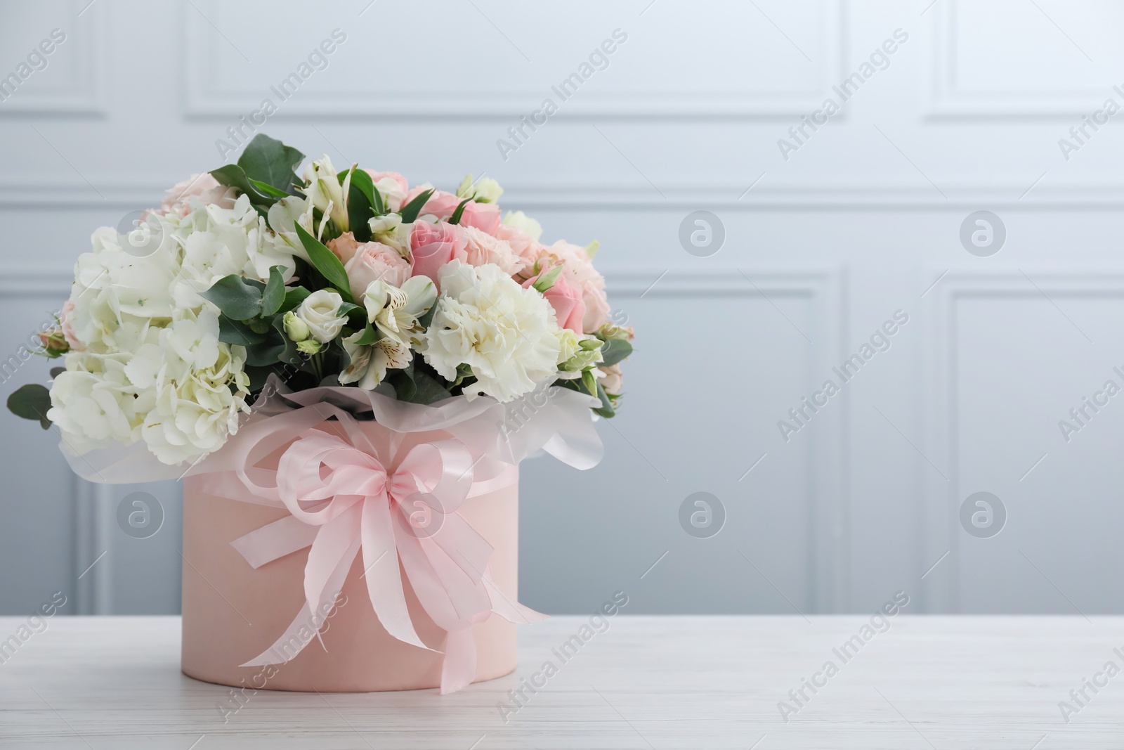 Photo of Beautiful bouquet in box on white wooden table. Space for text