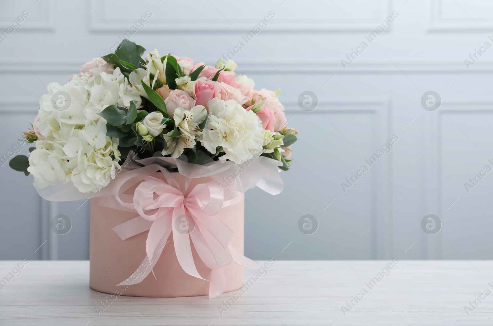 Photo of Beautiful bouquet in box on white wooden table against light wall. Space for text