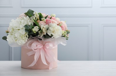 Photo of Beautiful bouquet in box on white wooden table against light wall. Space for text