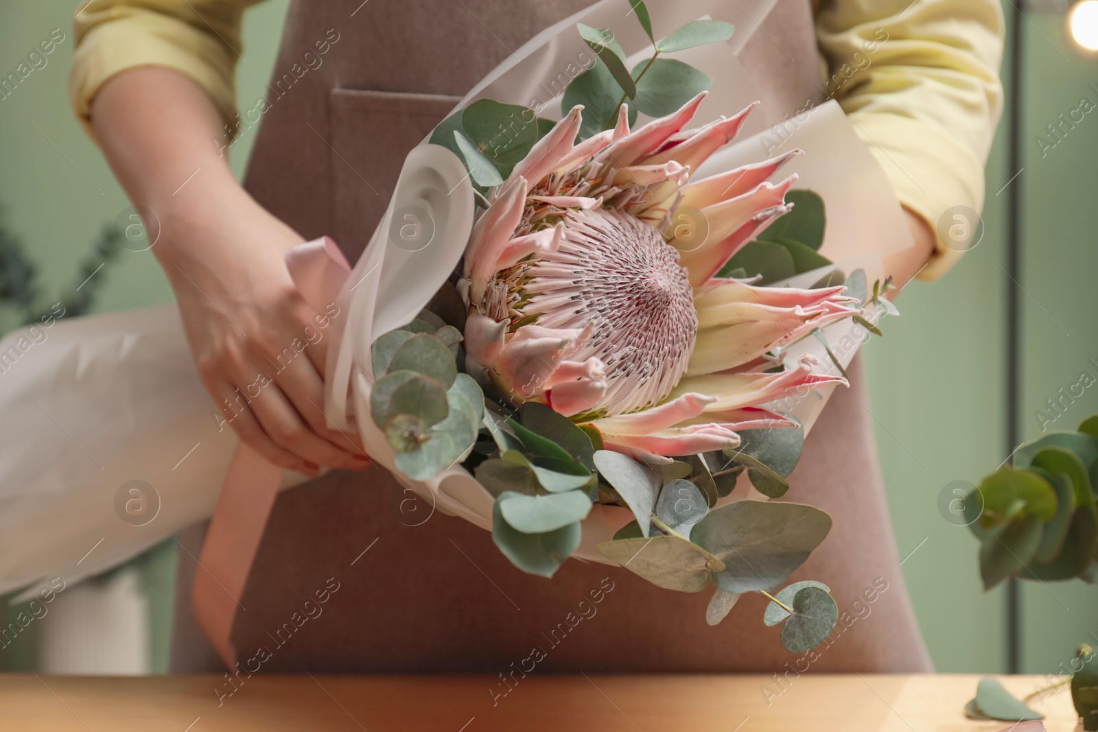 Photo of Florist with beautiful bouquet at table in flower shop, closeup