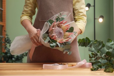 Photo of Florist with beautiful bouquet at table in flower shop, closeup