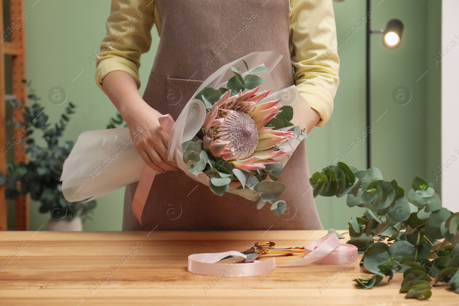 Photo of Florist with beautiful bouquet at table in flower shop, closeup