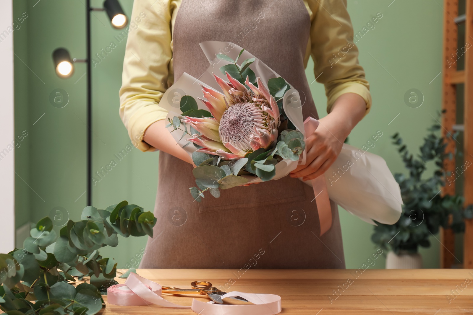 Photo of Florist with beautiful bouquet at table in flower shop, closeup