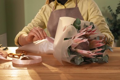 Photo of Florist making beautiful bouquet at table in flower shop, closeup