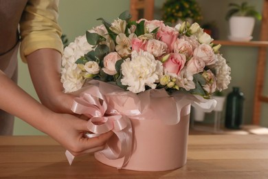 Photo of Florist with beautiful bouquet in box at table indoors, closeup