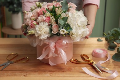 Photo of Florist with beautiful bouquet in box at table indoors, closeup