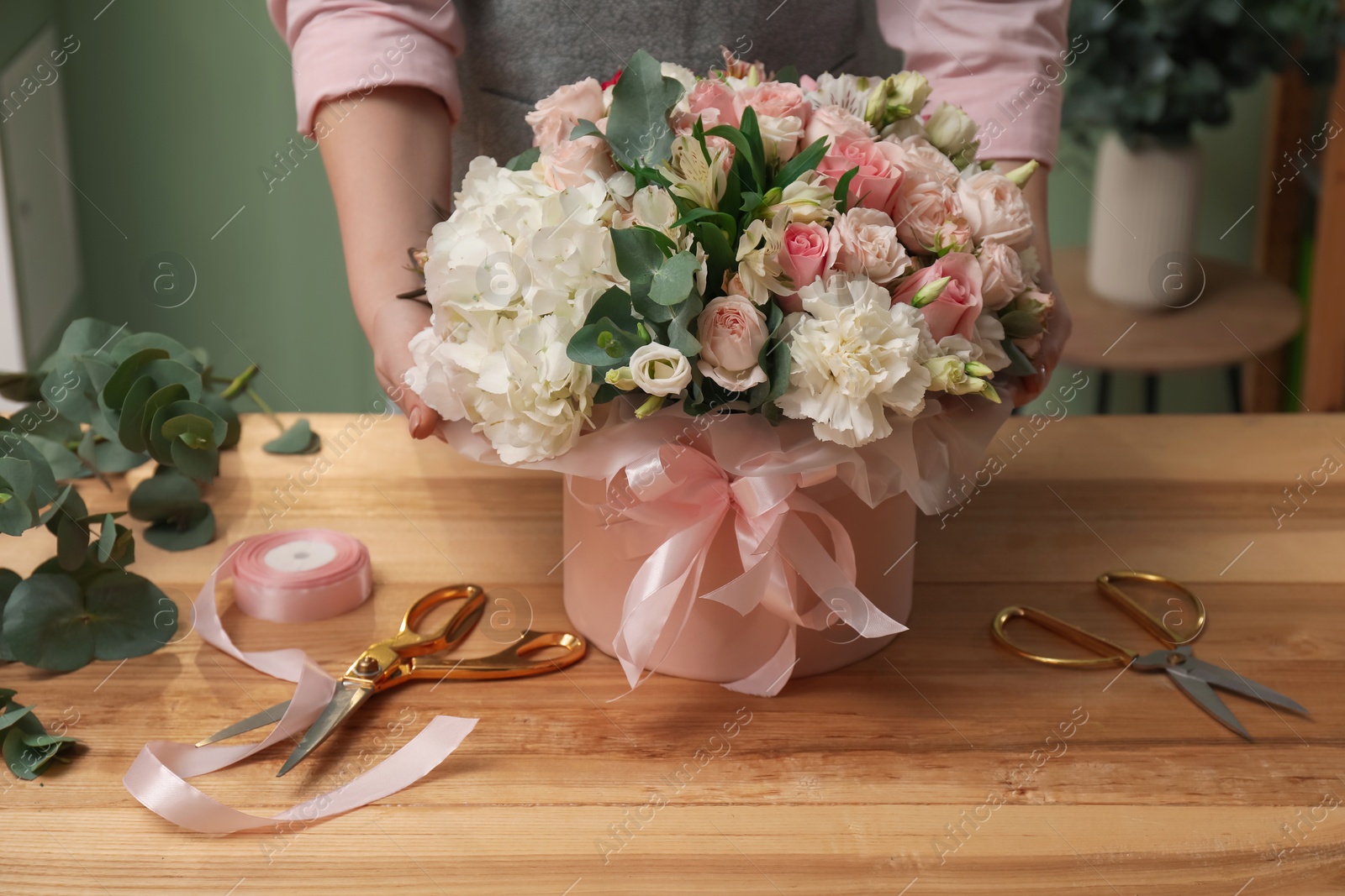 Photo of Florist with beautiful bouquet in box at table indoors, closeup