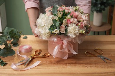 Photo of Florist with beautiful bouquet in box at table indoors, closeup