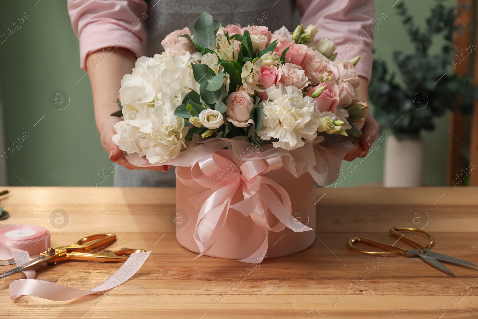 Photo of Florist with beautiful bouquet in box at table indoors, closeup