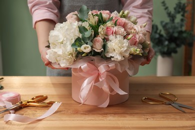 Photo of Florist with beautiful bouquet in box at table indoors, closeup