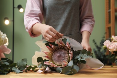 Photo of Florist making beautiful bouquet at table in flower shop, closeup