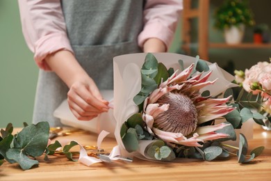 Photo of Florist making beautiful bouquet at table in flower shop, closeup