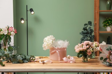 Photo of Beautiful flowers and box for bouquet on wooden table indoors