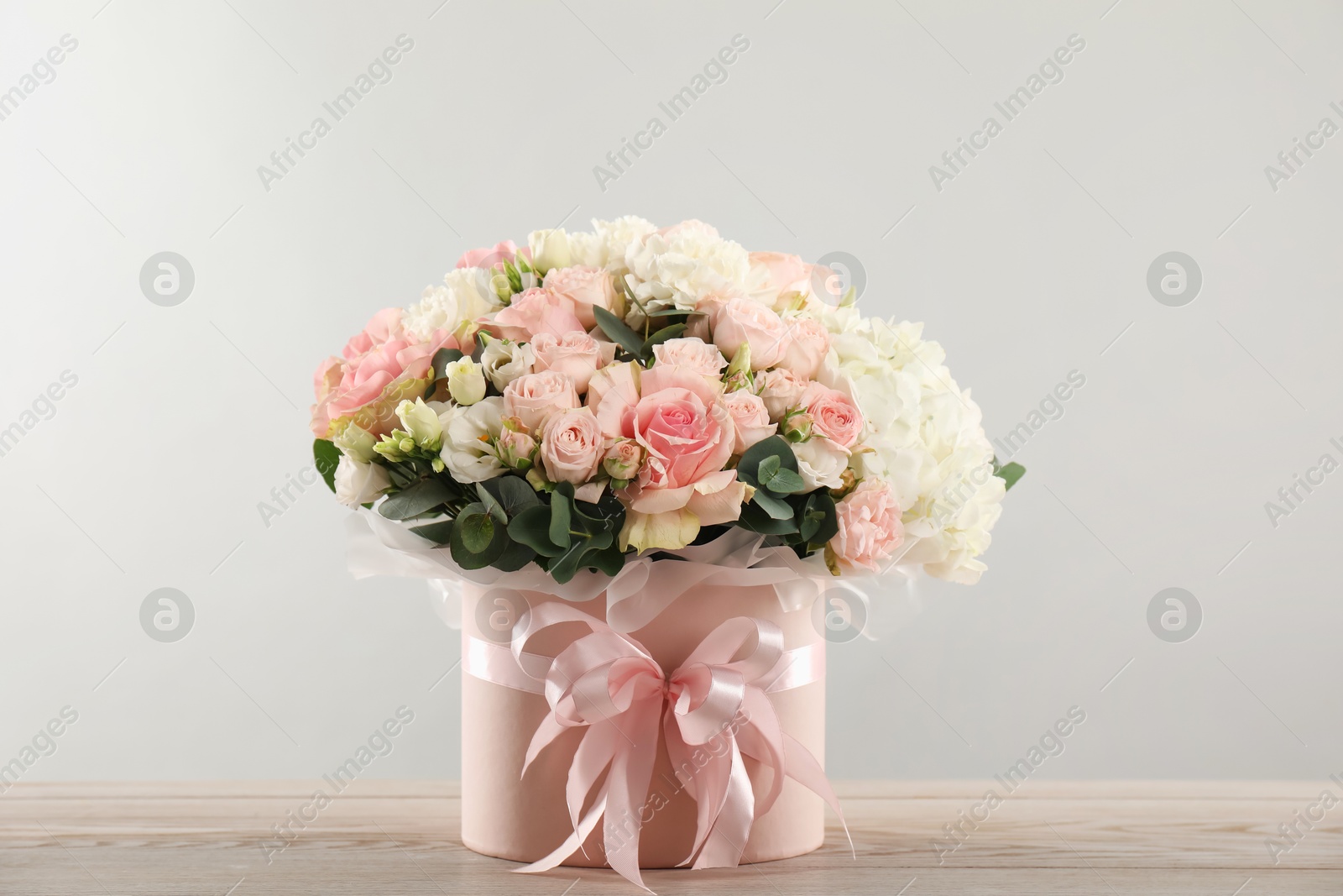 Photo of Beautiful bouquet in box on wooden table against light background