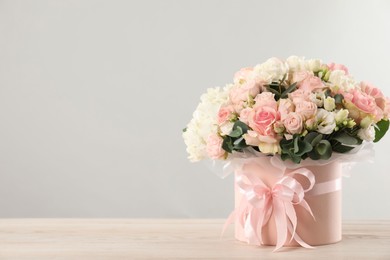 Photo of Beautiful bouquet in box on wooden table against light background. Space for text