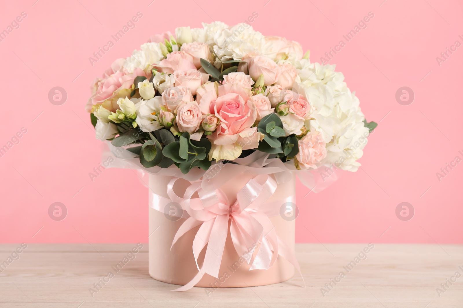 Photo of Beautiful bouquet in box on wooden table against pink background