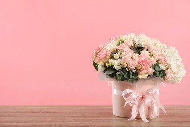 Photo of Beautiful bouquet in box on wooden table against pink background. Space for text